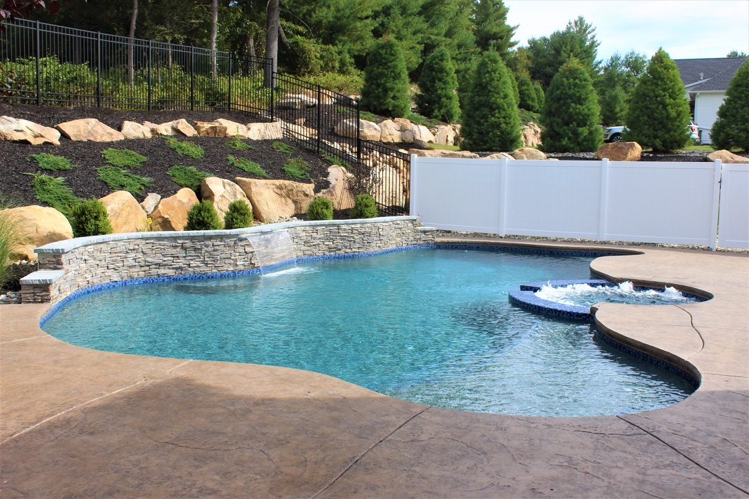 Custom freeform gunite pool with stone waterfall wall and attached spa