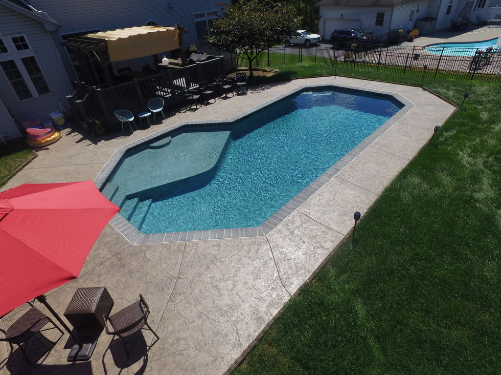 Custom geometric inground pool with stamped concrete deck — aerial view